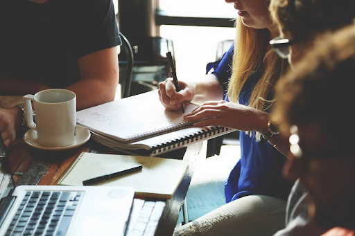 People sitting around a table with a mug, notebooks, and a laptop