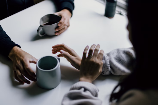 Two peoples hands on a desk both with coffee mugs