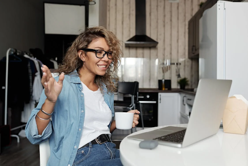 Woman with curly hair and black glasses, white shirt, denim jacket sitting at a desk in front of a computer